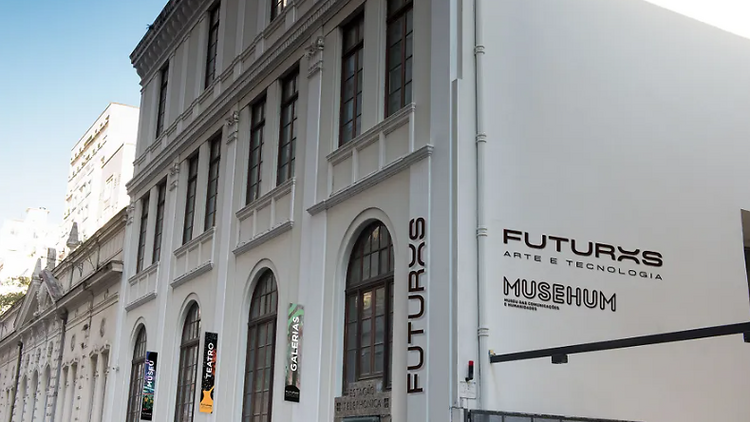 Fachada de um prédio branco com janelas marrons e o nome Futuros - Arte e Tecnologia escrito na lateral