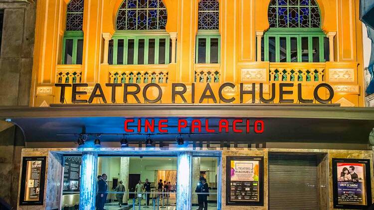 Fachada amarela do Teatro Riachuelo , sobre um letreiro neon escrito Cine Palácio