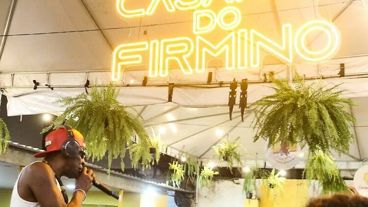 Um DJ anima o público logo abaixo de um letreiro iluminado que diz Casarão do Firmino