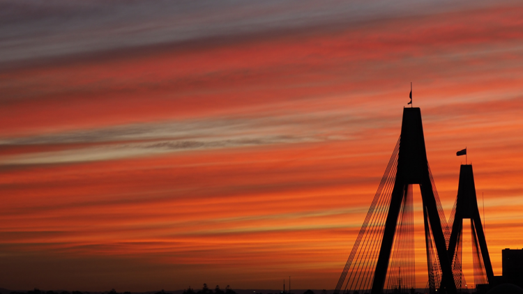 The top of the ANZAC Bridge against a red sky.