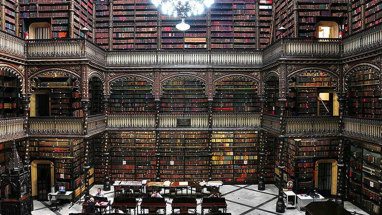 Vários andares com livros em todo o cumprimento das paredes, com um lustre pendendo do teto