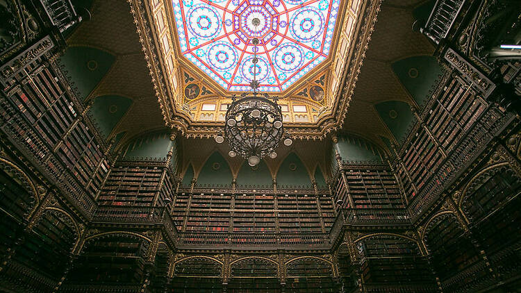 Imponente vitral colorido no teto do salão com livros por todas as paredes