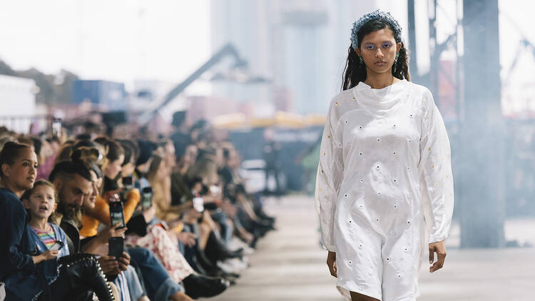 A model wearing a white dress walks on the runway. 