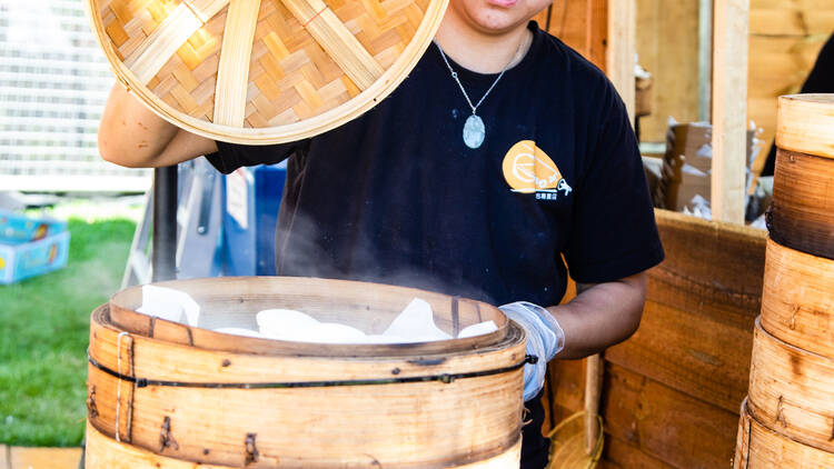 Worker lifting the lid of a steaming dumpling basket. 