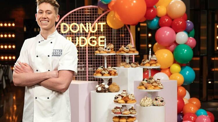 A smiling Morgan Hipworth standing in front of a doughnut display with balloons.