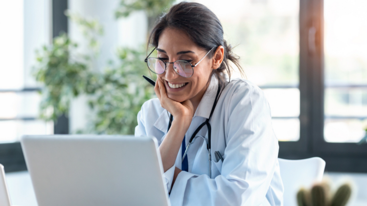 A doctor wearing a stethoscope sits looking at a laptop