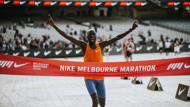 A marathon runner finishes with their arms raised in celebration. 