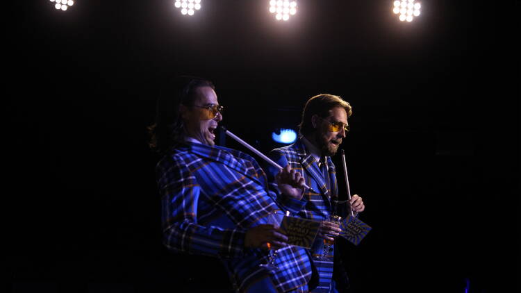 Two performers on stage in blue paid suits.