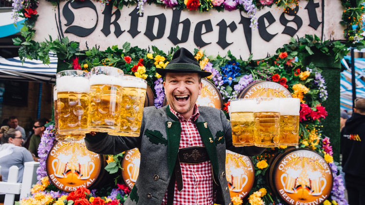 A man holding six steins of beer and wearing traditional German clothing. 