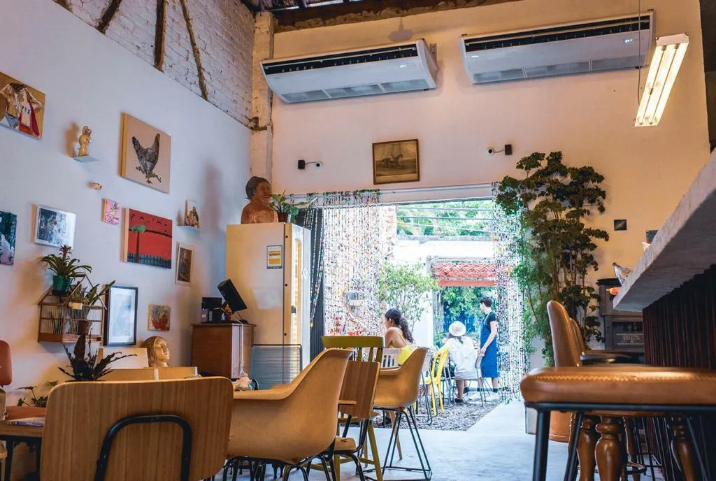 O interior do Quartinho Bar, com muitos quadros na parede, uma geladeira e, ao fundo, a área externa
