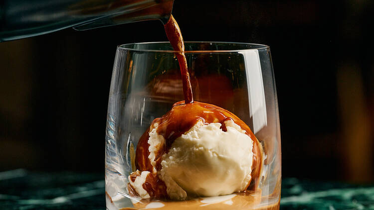 Barista creating an Affogato at a green marble espresso bar.