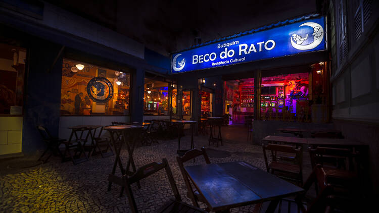 Frente do bar, com letreiro azul escrito Beco do Rato e mesas em área externa