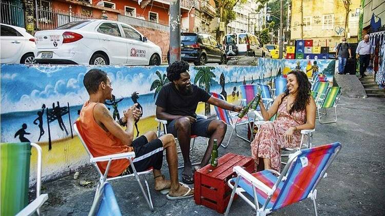 Três pessoas sentadas em cadeiras de praia em frente a uma mureta cheia de desenhos