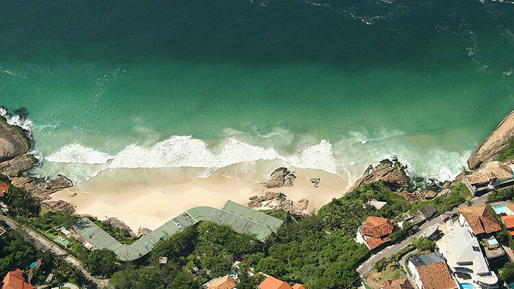 A Praia da Joatinga vista de cima, de um lado com águas esverdeadas, de outro com os casarões que ficam próximos