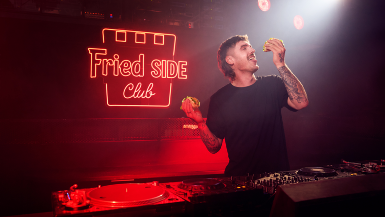 A DJ holding two sliders in a neon red room