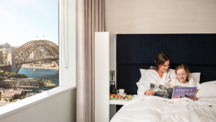A daughter and mum in bed at a hotel overlooking the harbour bridge