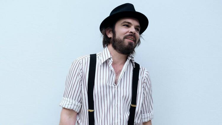 Gaz Coombes wearing a black hat, a white striped shirt and black braces