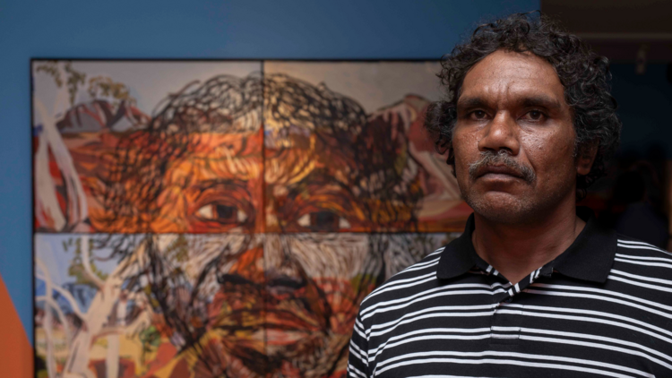Artist Vincent Namatjira stands with a self portrait