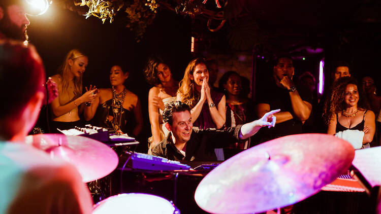 A performer plays instruments surrounded by a crowd.