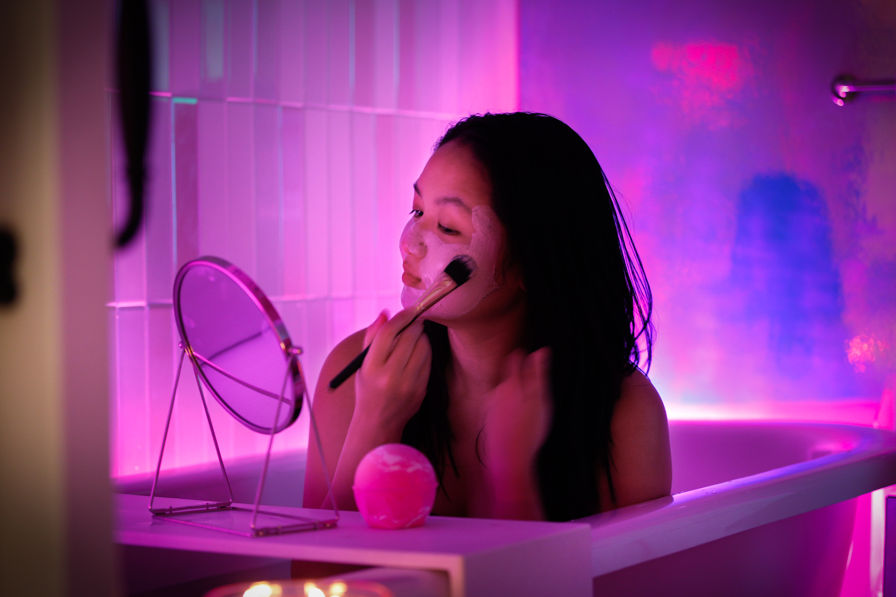 A woman sits in a bathtub while applying a face mask.