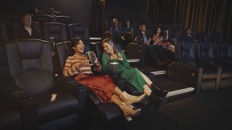 Two women in reclining seats in a movie theatre.