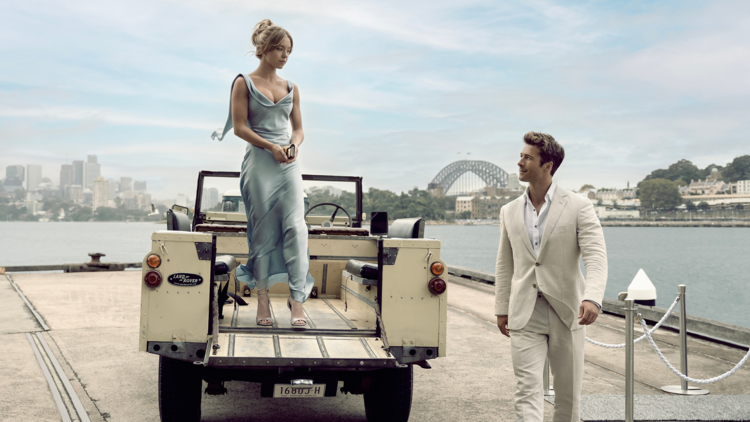 A woman on a jeep and a man in a suit pictured in front of the Harbour Bridge
