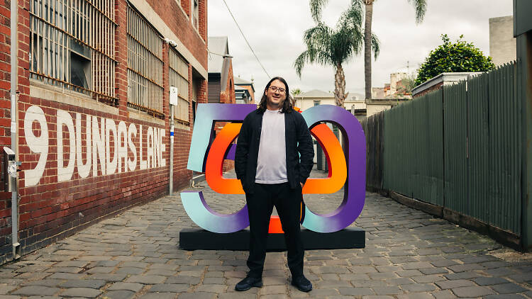 Matt Gudinski stands in front of a logo with the number 50 and a mushroom.