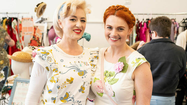 Two women in floral patterned dresses smiling. 