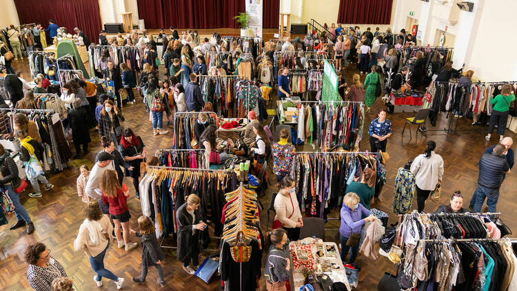 A room filled with clothing racks and people browsing. 