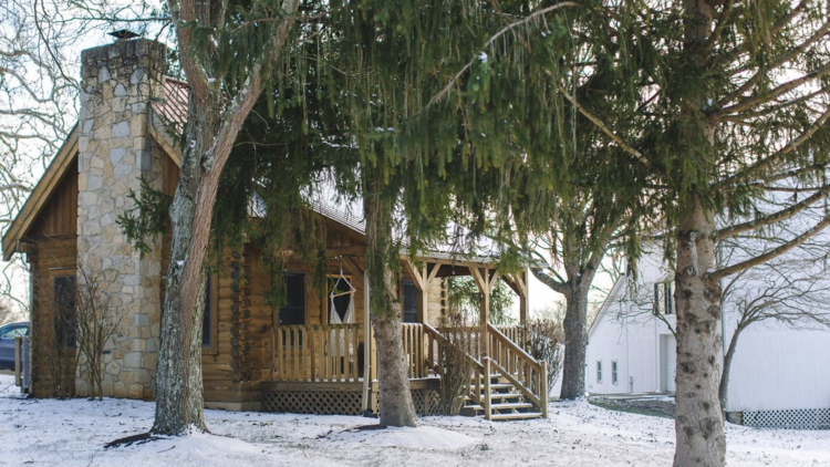 The exterior of a peaceful cabin in Cincinnati surrounded by snow and trees.