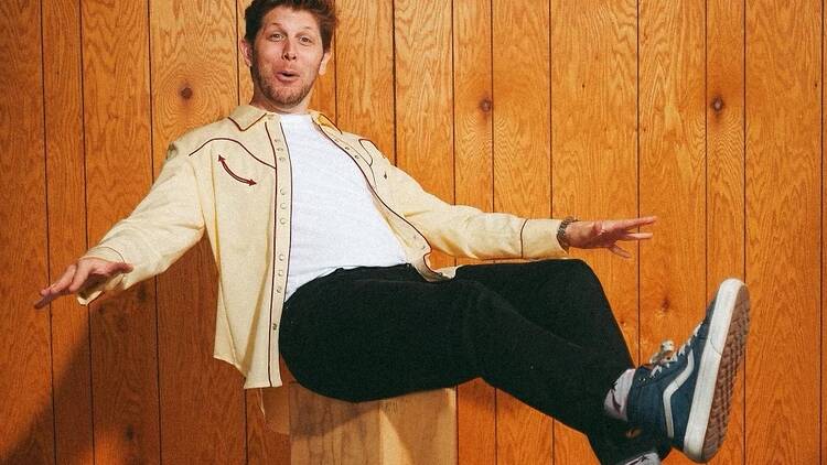 A man poses for a photo while sitting on a wooden stool.