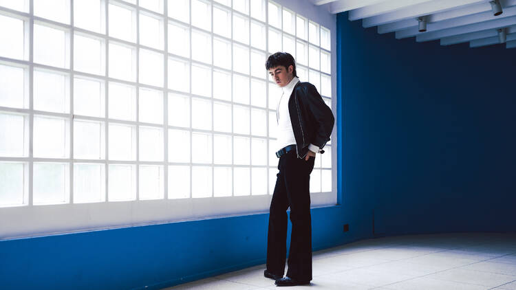 Picture of Declan Mckenna in black suit with blue room and light-filled window.