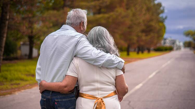 An old couple with grey hair who have their arms around each other. 