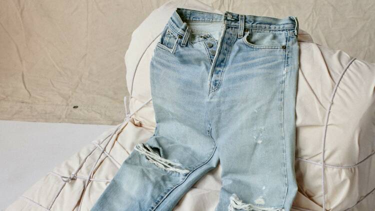 A pair of light blue distressed jeans with rips draped across an off-white chair