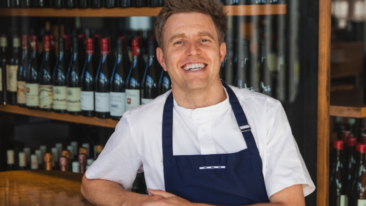Jason Staudt, executive chef at Stokehouse, posing in front of shelves of wine.