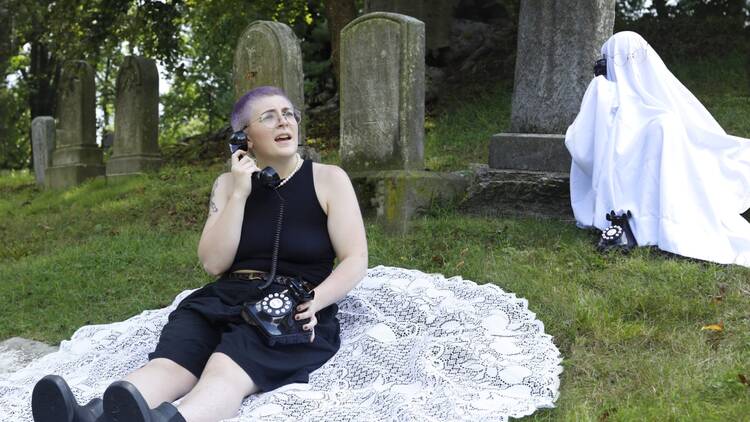 A person sits on a white lace blanket inside a cemetery.