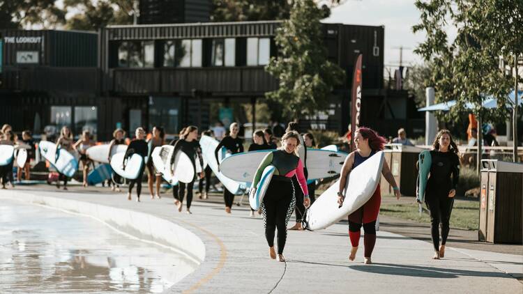 A group of women walking wearing wetsuits and holding surfboards. 