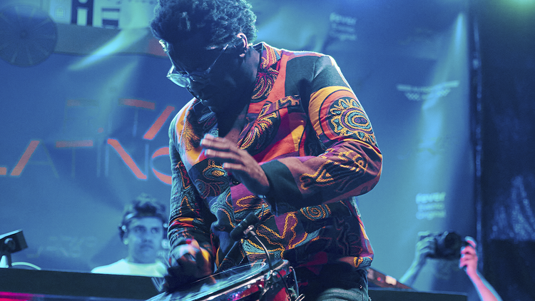 A man wearing a colourful shirt playing a drum on stage. 