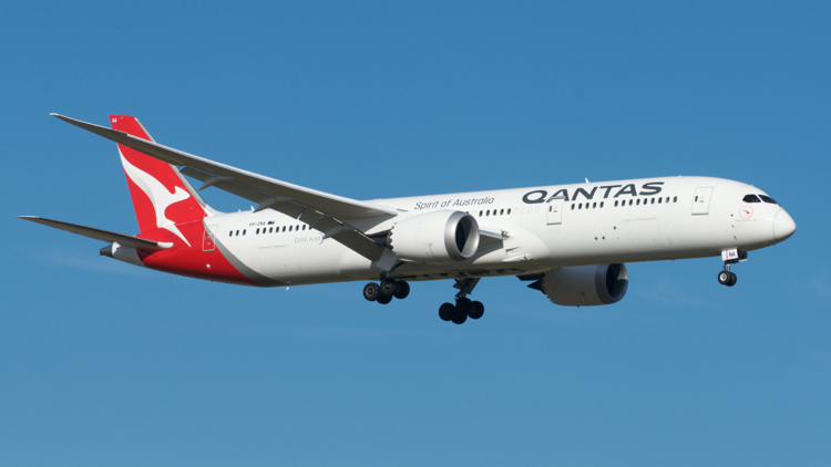 A Qantas plane flies in blue sky