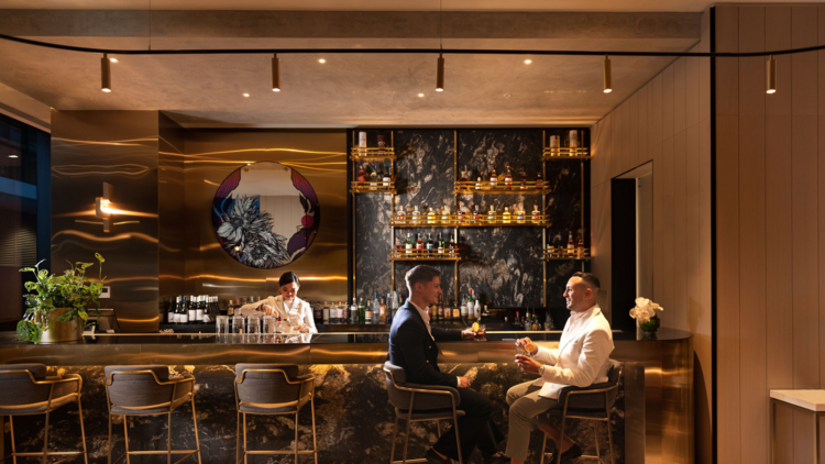 Two men sit in front of an elegant black and gold bar