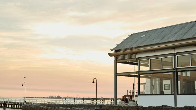 An exterior view of Pipi's Kiosk by the sea at dusk. 