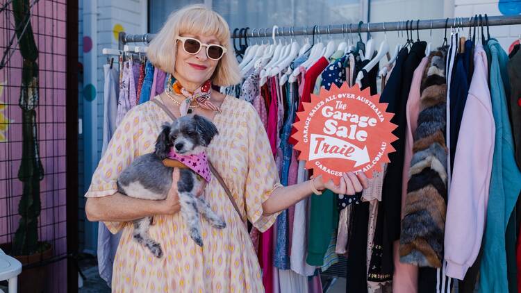 A woman holding a small dog and a sign that says Garage Sale Trail. 