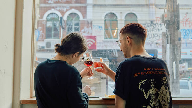 Two friends clinking drinks at Odd Culture in front of the window. 