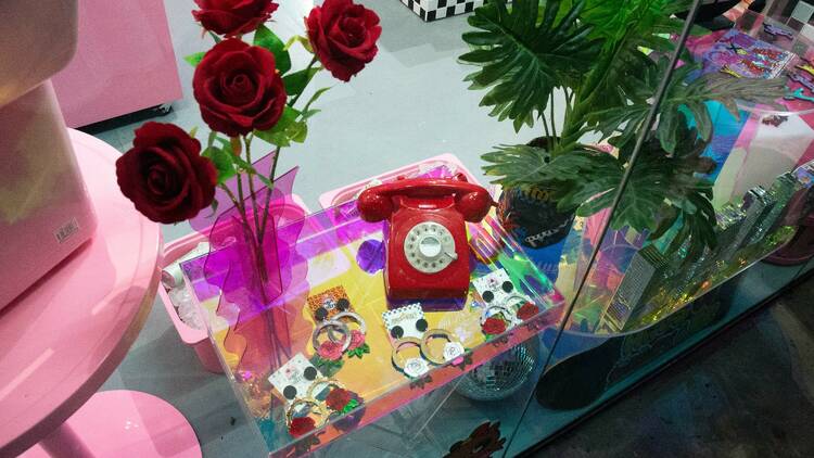 A table with brightly coloured earrings, flowers and a red old-fashioned telephone.