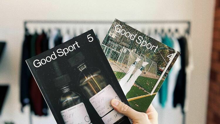 A hand holding two magazines with the words Good Sport on the front. 