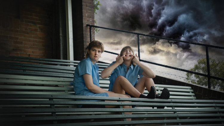 Two school children sitting in bleachers with a storm brewing