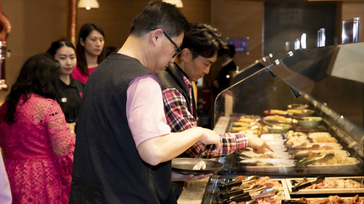 Man choosing raw cuts of wagyu beef from a buffet.