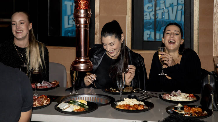 A trio of laughing women sitting at a table with various dishes of food. 