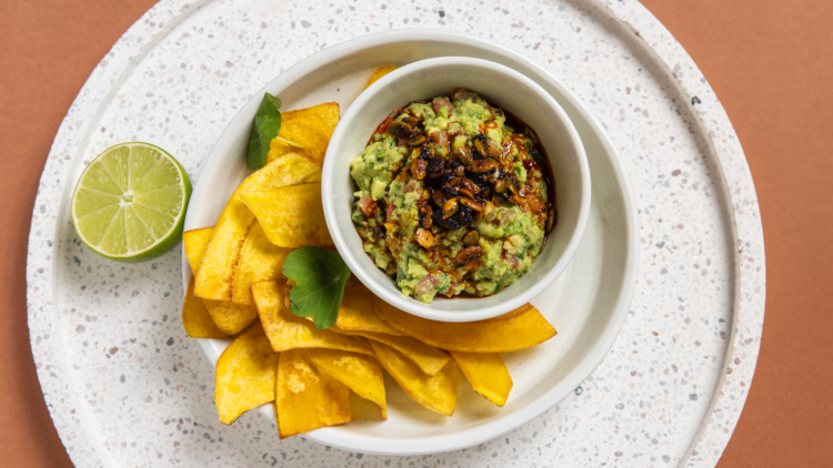 Nacho chips on a white plate with guacamole and lime