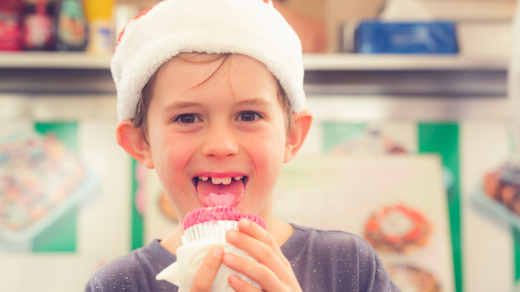 A boy wearing a Santa hat and eating a cupcake